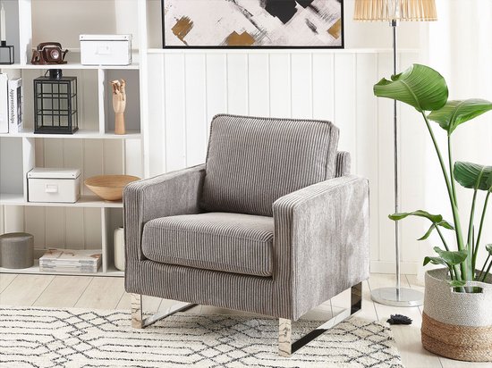 Lichtgrijze corduroy fauteuil in een modern interieur met open kast en plant.
