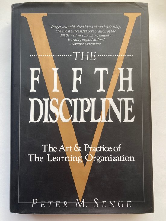 De kaft van het boek 'The Fifth Discipline: The Art & Practice of The Learning Organization' door Peter M. Senge. De kaft is zwart met een grote gouden 'V' en witte stippellijn. Titel in grote witte letters.