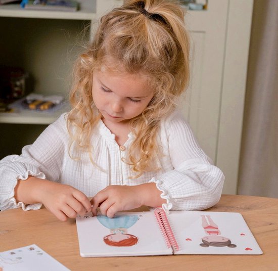 Blond meisje met krulletjes legt een sticker op een schetsboek met getekende meisjes.