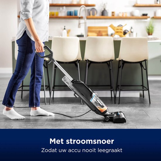 Een persoon met een wit shirt en spijkerbroek gebruikt de zwarte BISSELL CrossWave vloerreiniger met snoer in een keuken.