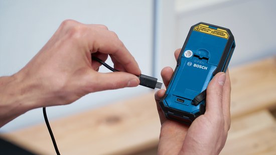 Hand sluit USB-kabel aan op de achterkant van de Bosch laser afstandmeter. Het apparaat is blauw met zwarte details.
