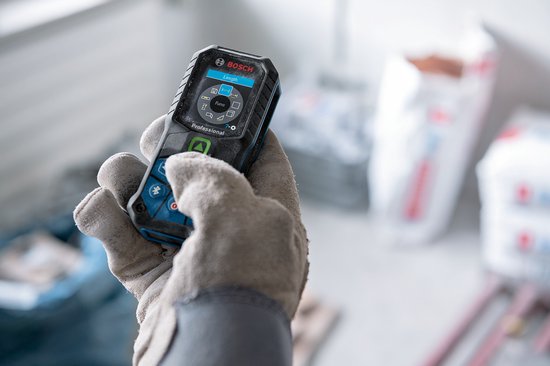 Hand met handschoen houdt Bosch laser afstandmeter vast. Het apparaat met groen en blauw accenten toont 'Lengte'.