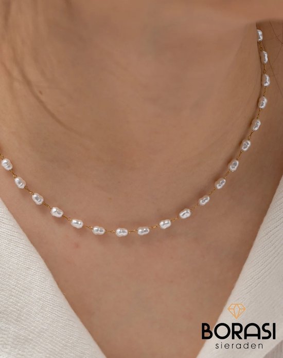 Gouden ketting met kleine, witte barokke parels gedragen door een vrouw.