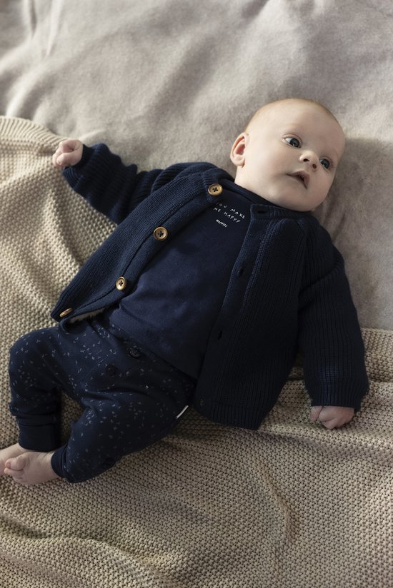 Baby in donkerblauw gebreid vest, donkerblauw shirtje met tekst en donkerblauwe broek met print.