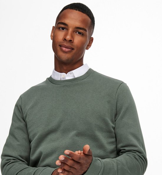 Man in een groene crewneck trui en wit overhemd.