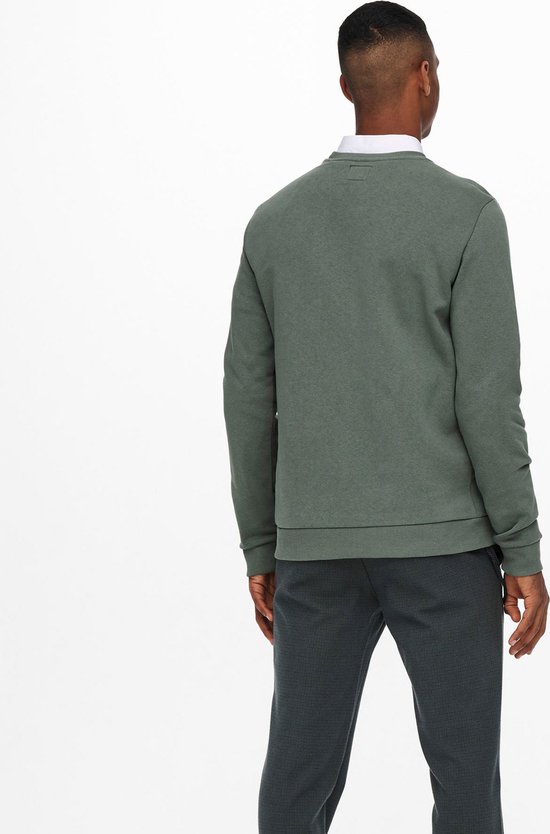Man in groene crewneck trui, wit overhemd en donkere broek, van achteren gezien.