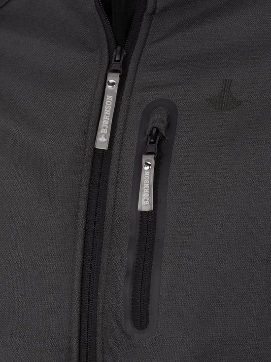 Detail van donkergrijze softshell jas met Bjørnson logoritsen op de borst en een klein logo op de stof.