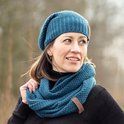 Een vrouw in een zwarte coltrui draagt een petrolblauwe gebreide muts en een bijpassende sjaal.