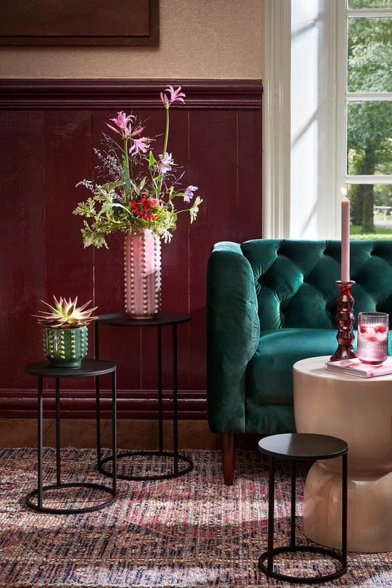Roze vaas met noppen en bloemen op een zwarte bijzettafel.