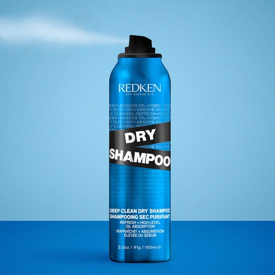 Een blauwe spuitbus Redken Dry Shampoo wordt gebruikt op haar, met een blauwe achtergrond.