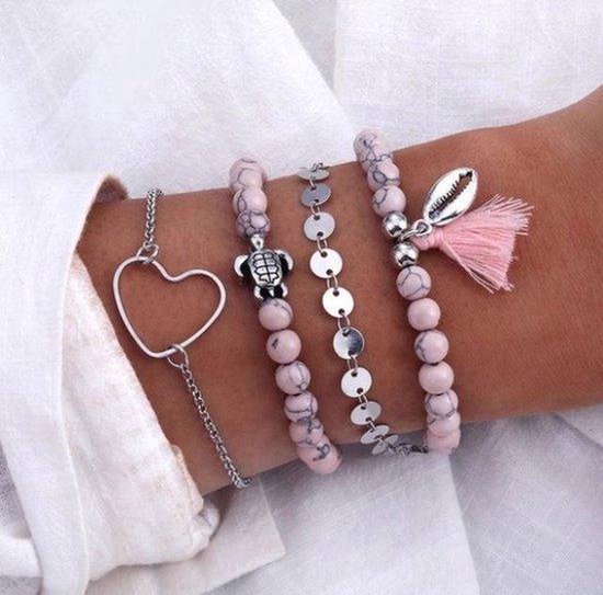 Set van vier armbanden gedragen op een arm: roze kralen met schelp en kwastje, zilverkleurige met schijfjes, en een met een hartje.