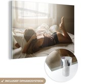 MuchoWow® Glasschilderij 90x60 cm - Schilderij acrylglas - Vrouw draagt lingerie in bed - Foto op glas - Schilderijen