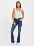 Model met donker haar draagt een beige tanktop en donkerblauwe flared jeans met lichte wassing.