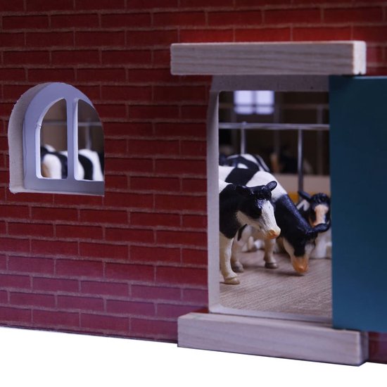 Detail van een speelgoedboerderij, met een raam en deuren, en zwart-wit koeien in de stal.