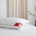 Een witte kussen met bruine bies ligt op een bed. Een rode "Canada Montreal" label en een wit label zijn zichtbaar.