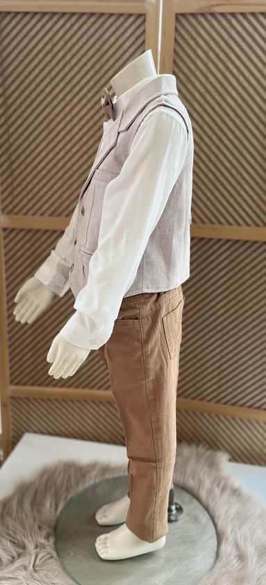 Zijaanzicht van een wit hemd met beige vest, bruine broek en bruine strik, gedragen door een mannequin.