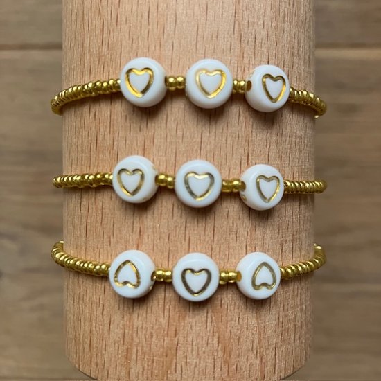 Drie gouden armbandjes met witte kraaltjes en gouden hartjes, geborduurd met kleine gouden kraaltjes.