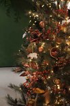 Detail van een kerstboom met dennentakken, dennenappels, bessen en kerstverlichting.