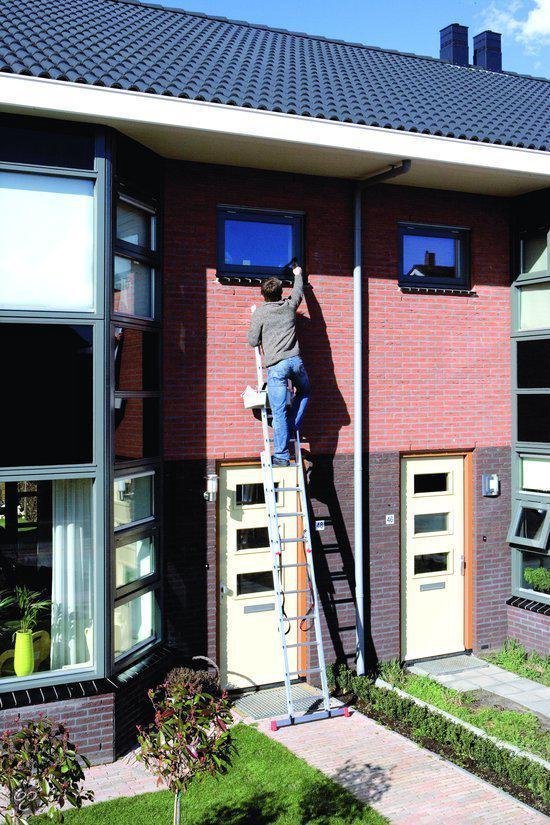 Man op een aluminium reformladder die een raam schoonmaakt van een bakstenen huis.
