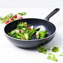 Zwarte wokpan met broccoliroosjes, peultjes en radijzen. Groene pan met wit handvat.