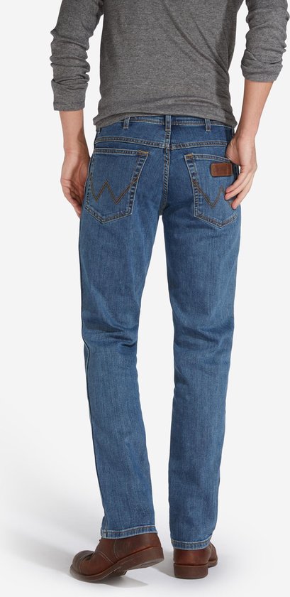 Achterkant van een blauwe regular fit jeans met bruine schoenen.