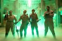 Vier vrouwen in Ghostbusters-uniformen staan in groene mist, gewapend met protonenpakken.