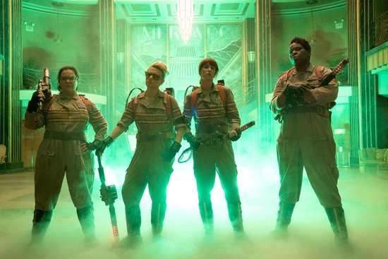 Vier vrouwen in Ghostbusters-uniformen staan in groene mist, gewapend met protonenpakken.