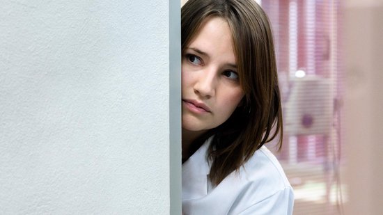 Close-up van een jonge vrouw die om een hoek kijkt, met een witte jas aan.