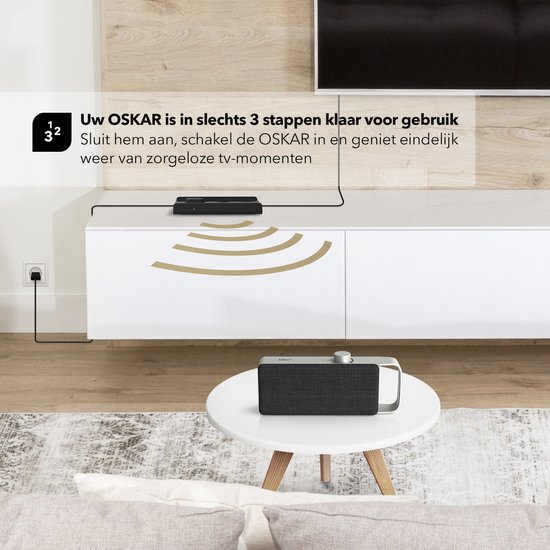 Een zwarte luidspreker met zilverkleurig handvat staat op een salontafel. In de achtergrond, een tv-meubel met een soundbar en een stekker in het stopcontact.