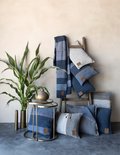 Blauwe en grijze kussens en plaids op een houten ladder, met een plant en bijzettafel.