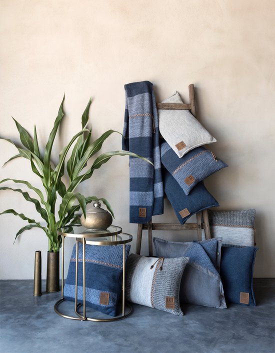 Blauwe en grijze kussens en plaids op een houten ladder, met een plant en bijzettafel.