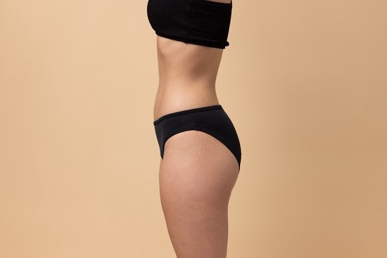 Vue de côté d'une femme portant un bas de bikini noir taille basse sur fond beige.