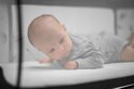 Baby in grijze kleding liggend op een wit matras in de wieg.