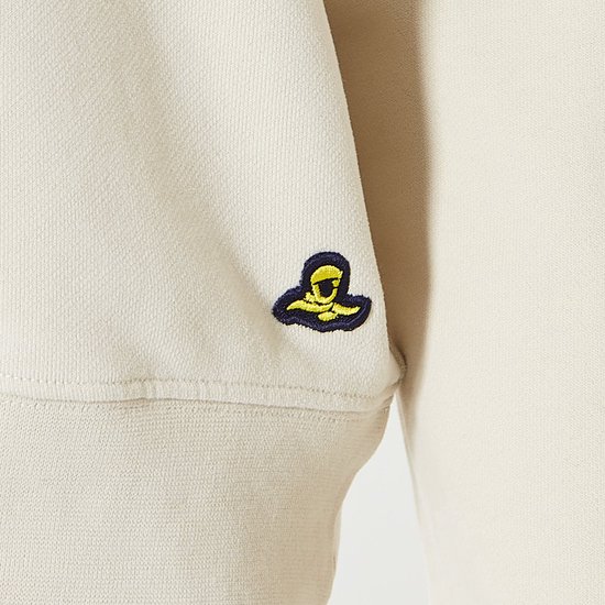Crème hoodie met een geborduurd geel-zwart logo op de mouw.