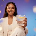 Une femme en tenue beige tient un verre côtelé rempli d'eau et de citron.