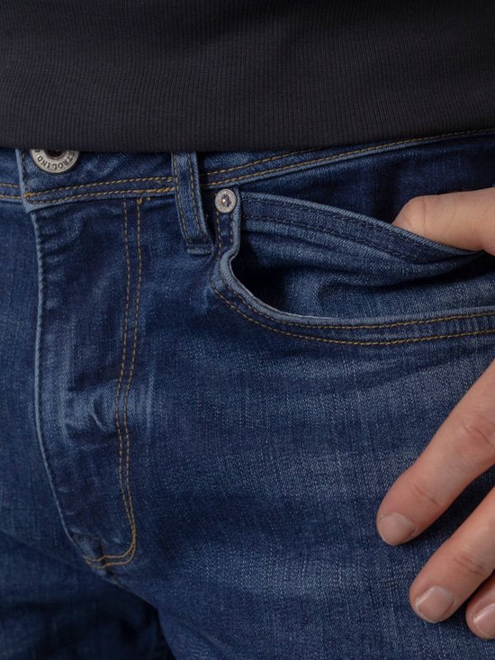 Detail van de zak van een donkerblauwe jeans met een bruine hand erin.