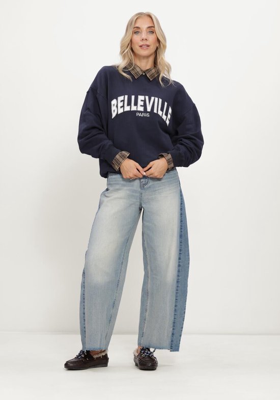 Model in een donkerblauwe trui met tekst en een wijde spijkerbroek met tweekleurig design.