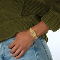 Goudkleurig Casio digitaal horloge met mesh-band, gedragen door een persoon in een olijfgroene trui en blauwe jeans.