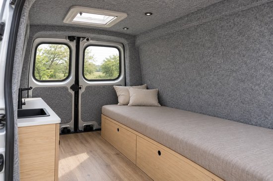 Camperinterieur met grijze viltwanden, houten meubels, een ligbed en een keukengedeelte.