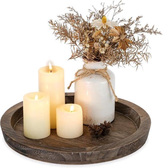 Rond donkerhouten dienblad met drie crèmekleurige kaarsen, een wit vaasje met droogbloemen en dennenappels.