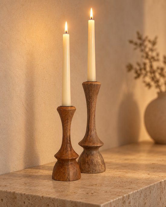 Twee brandende kaarsen in houten kandelaars op een natuurstenen plank tegen een beige muur.
