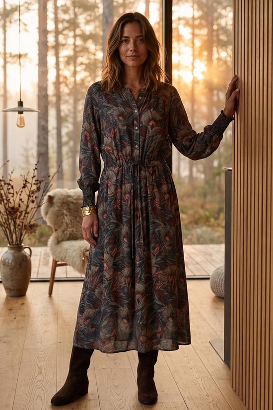 Vrouw in midi-jurk met donkerbruine botanische print, knoopsluiting en geplooide mouwen in een bosrijke setting.