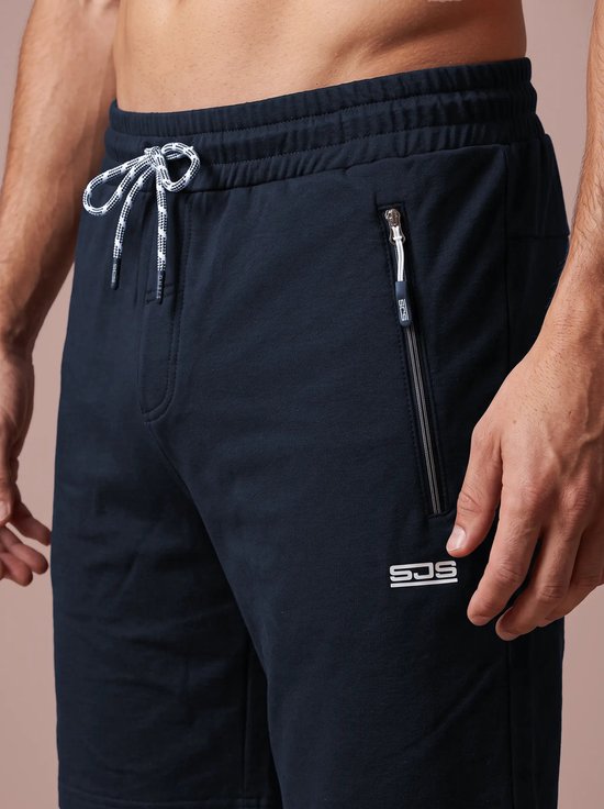 Close-up van marineblauwe sportshort met wit trekkoord, ritszak en wit SJS-logo op het bovenbeen.