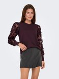 Model in een wijnrode trui met lange mesh mouwen met bloemapplicaties.
