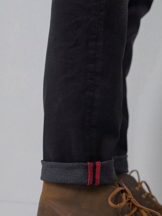 Donkergrijze jeans met omgeslagen pijpen met rode accenten en bruine schoenen.
