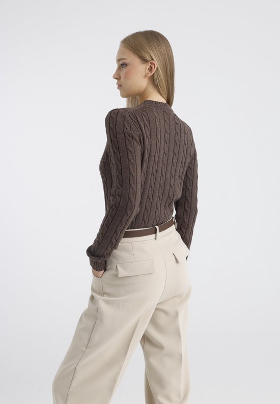 Model met bruine kabeltrui en beige broek, staand opzij.
