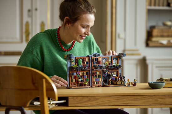 Een vrouw met een groene trui en rode ketting houdt de LEGO Boekhandel vast en bekijkt deze aandachtig.