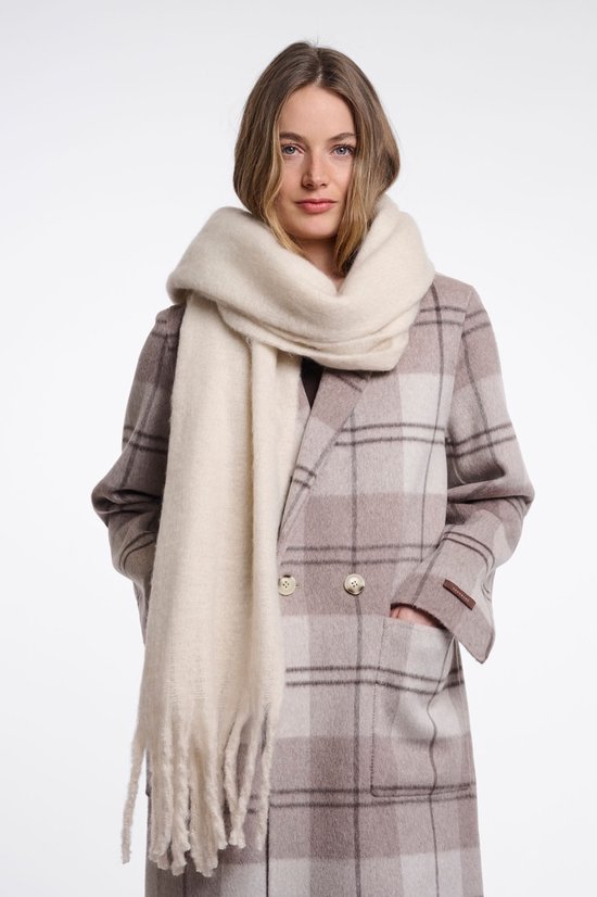 Model draagt een beige geruite jas met crème gebreide sjaal met franjes.