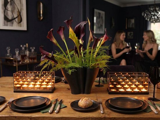 Een gedekte tafel met twee kandelaars, een zwarte vaas met calla lelies en place settings.