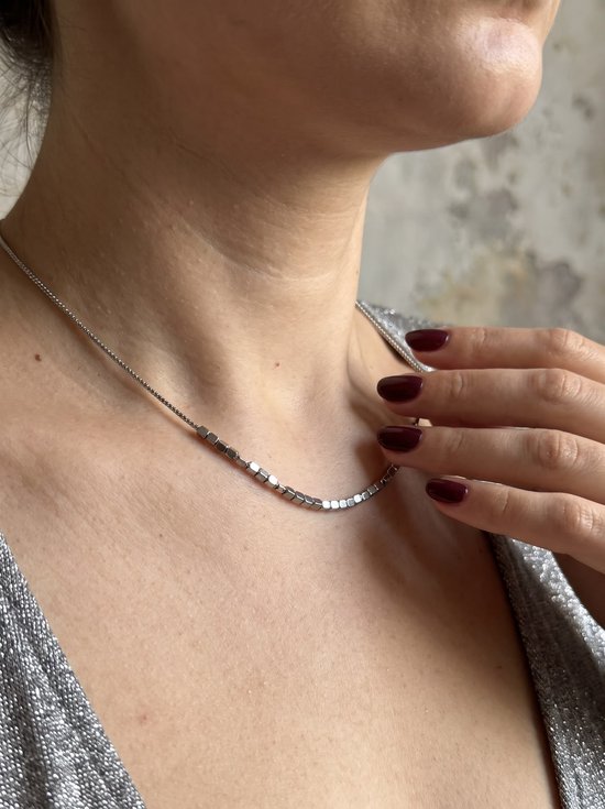 Zilverkleurige ketting met kleine vierkante kralen, gedragen door een persoon met een zilveren topje.
